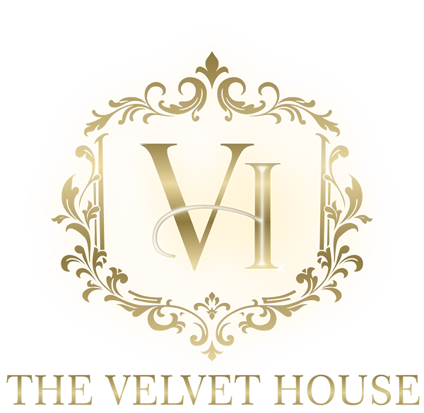 Gold ornate crest with the large, stylised letters VI in the centre, surrounded by decorative flourishes. Below the crest, gold text reads THE VELVET HOUSE on a light background.